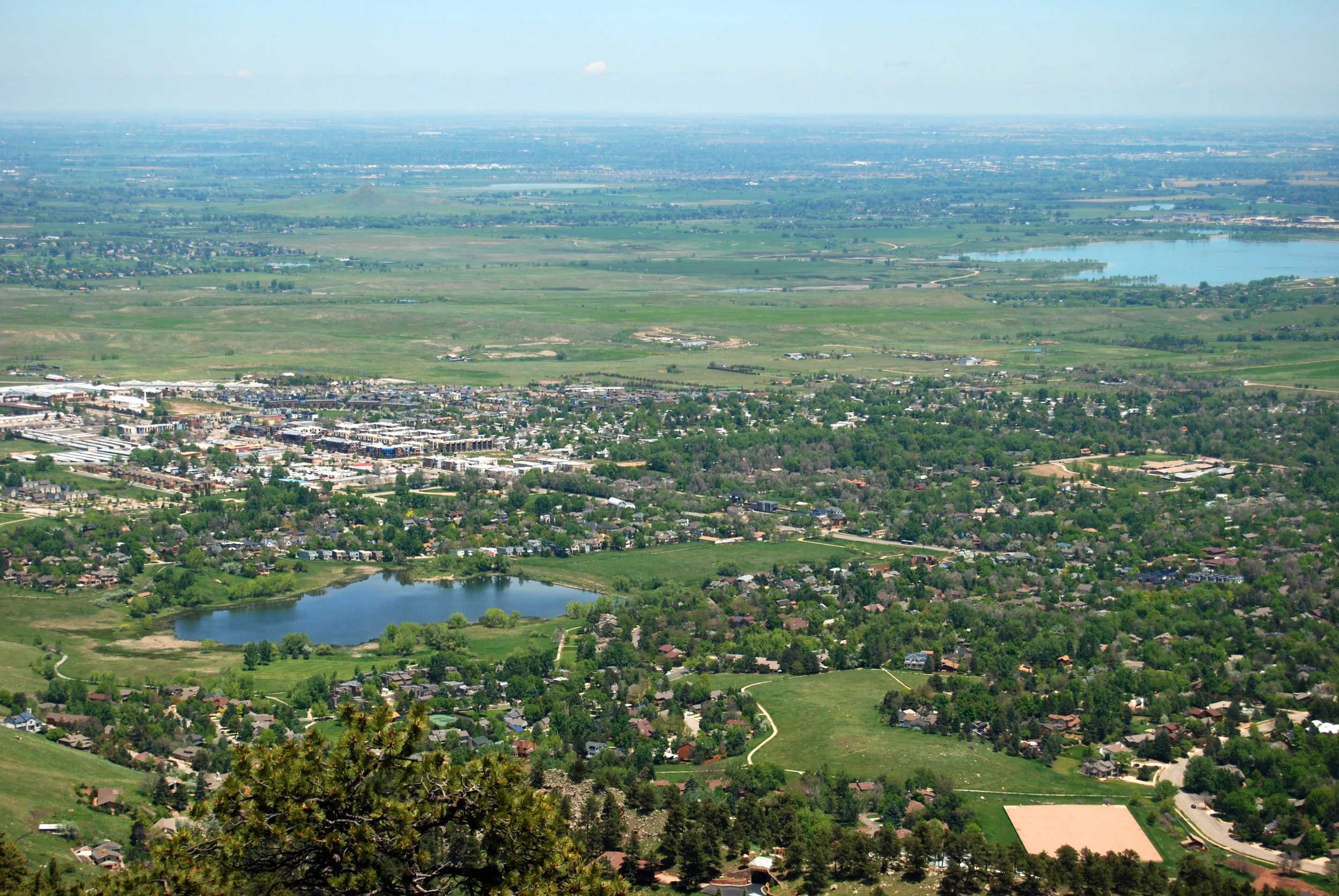 Aerial photograph of a green suburban town with scattered lakes, trees, and buildings under a hazy blue sky, calm and expansive mood