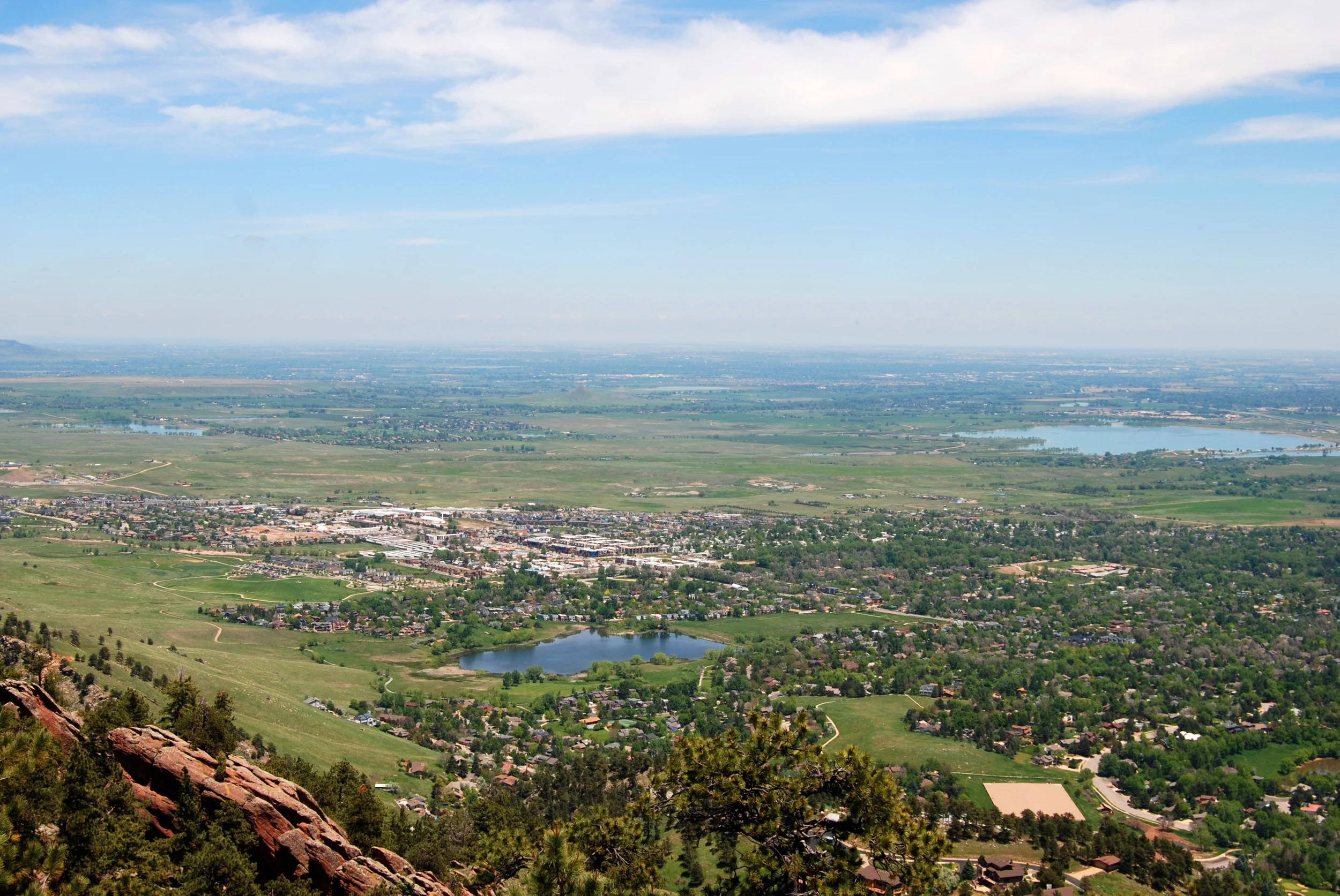 Aerial view of a small town nestled among green plains and small lakes with mountains in the distance under a hazy blue sky, scenic and quiet mood