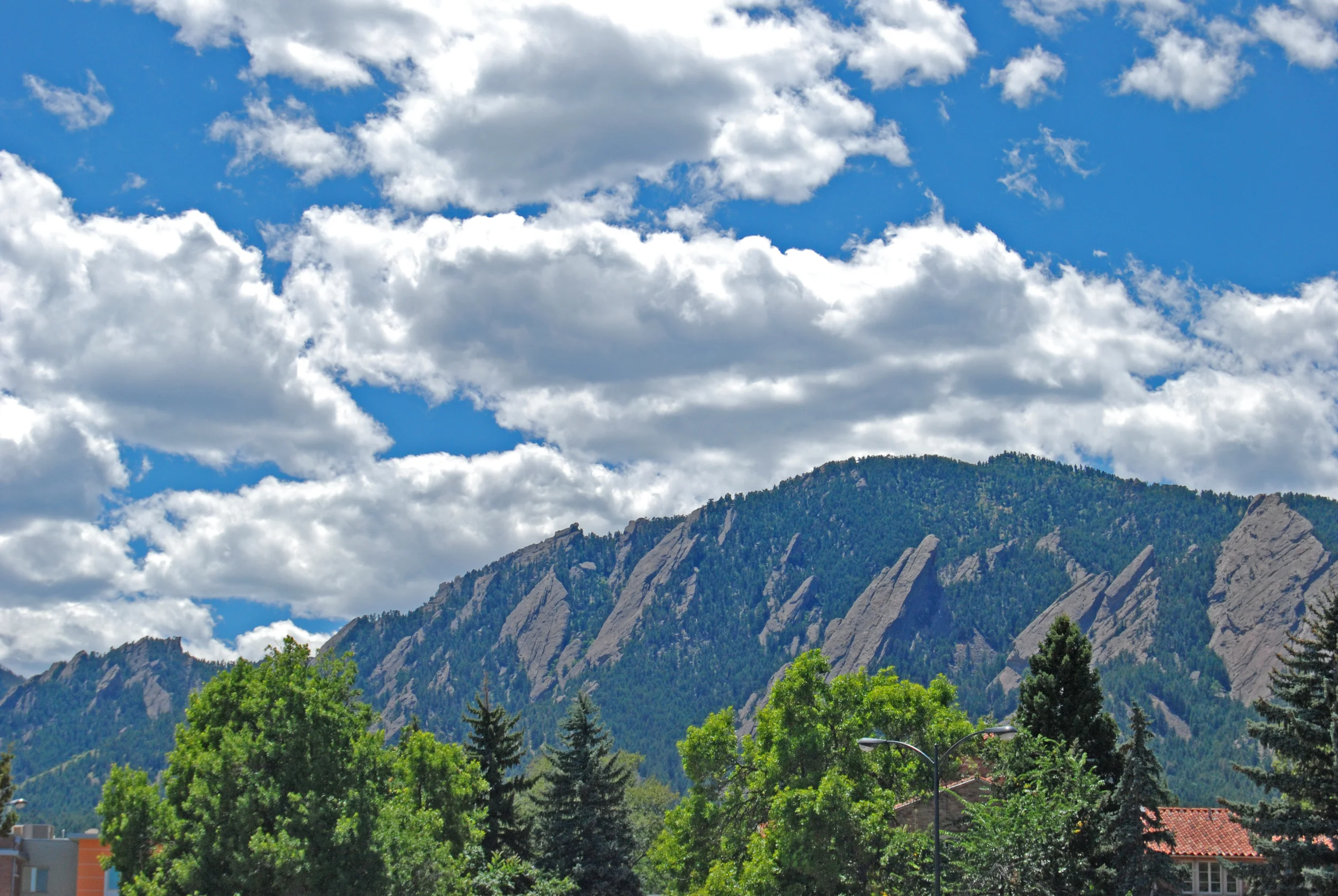 Rocky mountain formation with green trees in the foreground and a blue sky with clouds, bright and natural daytime mood
